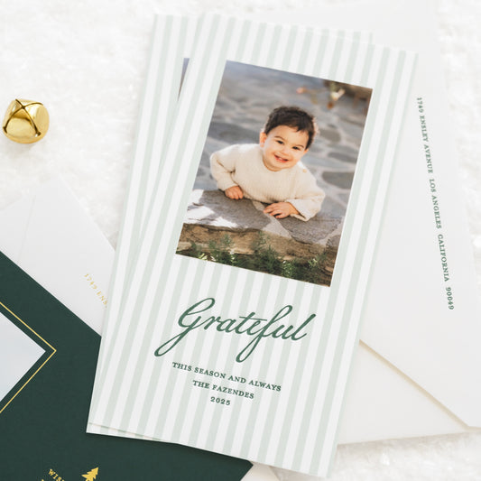 Close up of mint green striped custom holiday photo card with little boy and pine green printed 'grateful this season and always' paired with a white envelope