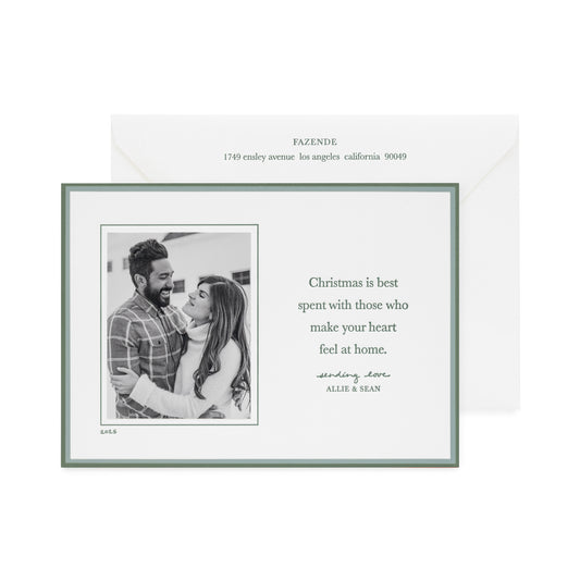 Custom holiday photo card with a black and white photo with a double green border on a white card with green letterpress ink messaging 'christmas is best spent with those that make your heart feel at home' paired with a white envelope with matching green ink with address