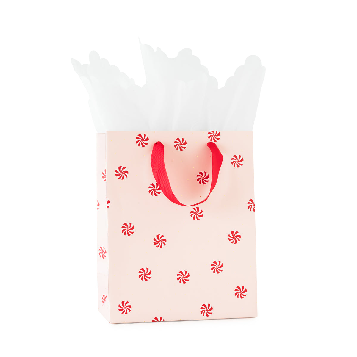 A light pink gift bag with red handles and a repeating red peppermint candy print, filled with white tissue paper
