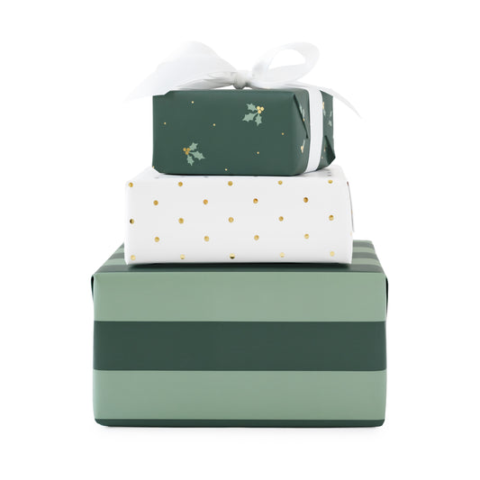 a stack of three wrapped gifts - one with thick mint and evergreen stripe wrap, one with white with gold foil swiss dots, and one that is evergreen with mint and gold foil holly berry and leaves tied with a white bow on top
