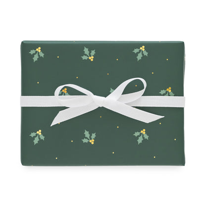 A rectangular gift box wrapped in dark green holiday paper with a white ribbon bow, featuring a pattern of small holly leaves, gold berries, and gold dots