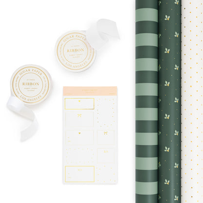 A flat-lay product of gift wrap items including two rolls of ribbon, a sheet of gift stickers, and three rolls of patterned wrapping paper on a clean white background. One roll is a dark green and mint stripe, one is green background with mint green holly and gold dots and a white with gold swiss dot pattern