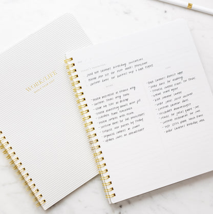 An open white spiral notebook with gold wire binding, showing lined pages with gold foil text reading 'WORK LIFE' and handwritten notes with prompts of 'today's priorities,' 'work,' and 'life'