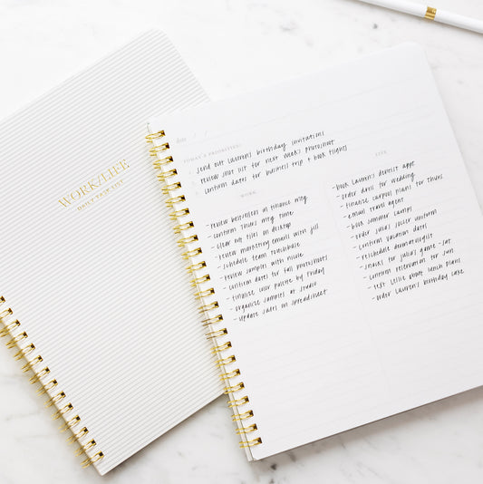 An open white spiral notebook with gold wire binding, showing lined pages with gold foil text reading 'WORK LIFE' and handwritten notes with prompts of 'today's priorities,' 'work,' and 'life'